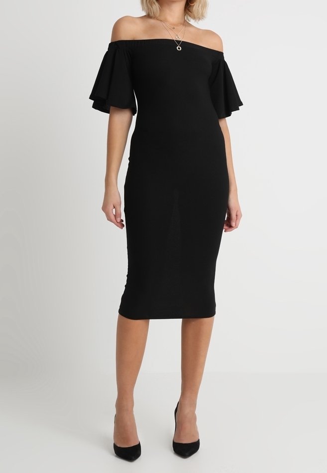 Robe noire à épaules dénudées avec manches courtes évasées, silhouette ajustée et longueur au genou. Texture lisse, associée à des talons hauts noirs.