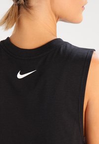 Espalda superior de una mujer que lleva una camiseta sin mangas negra de Nike con el logo blanco de la marca debajo del escote.