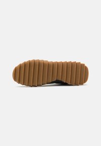 Suela de zapato negra con surcos en patrón, con el texto "new balance" embellecido. Material de goma duradero, diseñado para tracción y agarre.