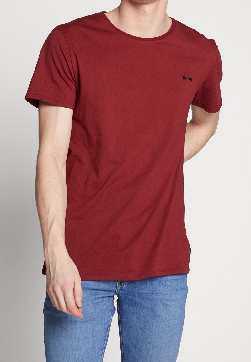 Maronfarvet t-shirt med korte ærmer i blødt bomuldsstof med rund hals og diskret logo detalje på brystet. Parret med lyseblå jeans.