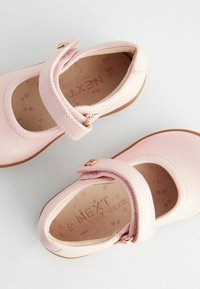 Rosa läderskor för första steg med rund tå, justerbar rem och beige gummisula. Inuti finns ett mönster av ljusa tassavtryck.
