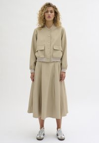 Beige two-piece outfit featuring a cropped bomber jacket with snap buttons and two front pockets, paired with a flowing midi skirt.