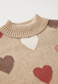 Pulover bej cu guler rib accesorizat cu diverse modele de inimi în nuanțe de roșu, maro și alb. Textură moale de tricot pe toată suprafața.