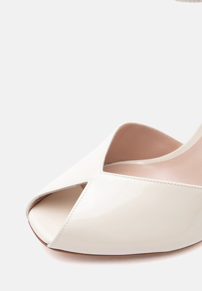 Λευκό τακούνι από δέρμα λάκας με ανοιχτό δάχτυλο, σχέδιο σταυρωτού και λείο εσωτερικό επένδυμα σε απλό φωτεινό φόντο.