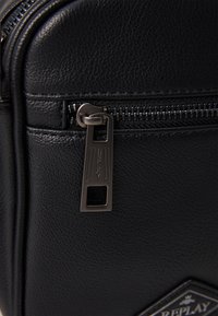 Black synthetic leather bag featuring a smooth texture, a metallic zipper with a rectangular pull, and a diamond-shaped logo patch.