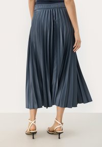 Jupe midi plissée en satin bleu marine, dotée d'une taille élastique et d'une texture lisse et fluide. Associée à des talons beiges à lanières.
