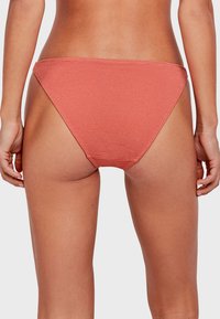 Bikini in tessuto a coste di un delicato corallo. Design a vita bassa con copertura minima e sottili cinturini laterali. Texture liscia e finitura senza cuciture.
