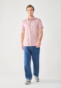 Camisa corta de manga larga color rosa claro, hecha de una tela de textura suave, combinada con unos jeans de denim azul sueltos y zapatillas grises.