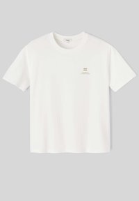 T-shirt en coton blanc à manches courtes et encolure ronde, avec une petite vague dorée et du texte imprimé sur le côté gauche de la poitrine.