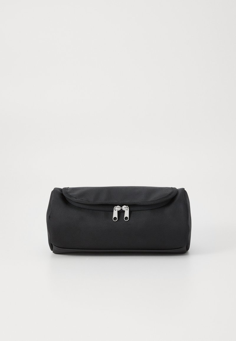 Black cylindrical bag made of textured fabric, featuring a flap closure and two silver zipper pulls. Compact design, no visible patterns.