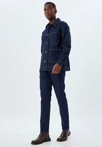 Set in denim composto da giacca e pantaloni, di colore indaco scuro, con chiusura a bottoni, due tasche sul petto e design a gamba diritta. Stivali in pelle completano l'outfit.