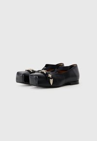 Black leather flats with a rounded toe, featuring silver decorative hardware and elastic straps. Smooth texture and minimalistic design.