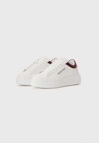 Witte leren sneakers met een dikke witte zool, voorzien van een bordeauxrode hielaccent en logo details aan de zijkant. Glad textuur, vetersluiting ontwerp.