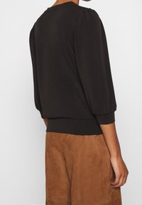 Black puff-sleeve top with a rounded neckline, soft fabric, and stretchy waistband, paired with brown suede shorts.