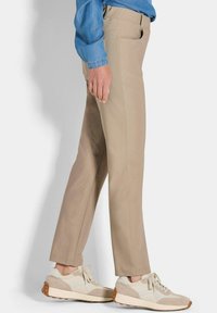 Beige rechte broek met zijzakken, gecombineerd met lichtgrijze sneakers met een textuurzool, en een blauwe denim overhemd.