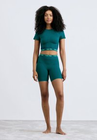 Mėlynas Calvin Klein aktyviosios aprangos komplektas, kuriame yra prigludęs trumpas topas ir šortai, pagaminti iš minkštos medžiagos su logotipo juostele ties liemeniu.