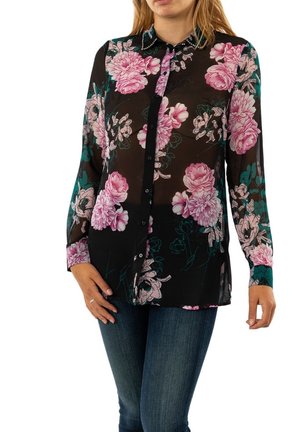 Donna che indossa una blusa nera trasparente con stampa floreale rosa e maniche lunghe, abbinata a jeans blu.