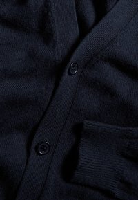 Navyblaue Strickjacke aus strukturiertem Stoff mit gerippten Bündchen und drei dunklen Knöpfen entlang der Vorderseite.
