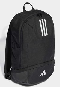 Schwarzer Rucksack aus strapazierfähigem Stoff, mit einem Hauptfach mit Reißverschluss, einem Seitennetzfach und einem Design mit drei weißen Streifen.