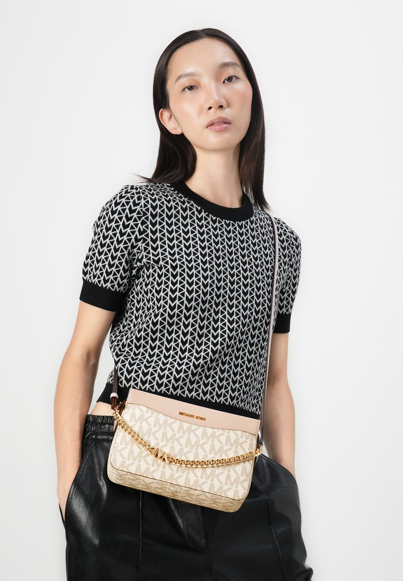 Borsa a tracolla beige con tracolla in catena dorata e motivo logato, completata da un top in maglia geometrica bianco e nero. Pantaloni in pelle eleganti completano il look.