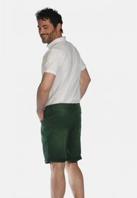 Shorts en denim verts avec un ourlet retroussé, poches arrière et un polo blanc ajusté. Les shorts ont une texture lisse et un design sur mesure.