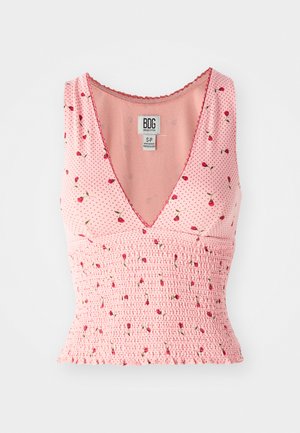 Pink sleeveless top with a V-neck, featuring smocked detailing and a floral print. Small red flowers are scattered on a polka dot background.