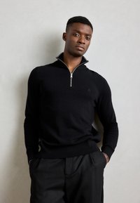 Zwarte zip-neck trui gemaakt van zachte stof, met een slanke pasvorm, lange mouwen en een geribbelde zoom met subtiele logo-details.