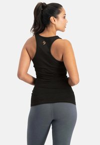 Schwarzes Sporttanktop mit figurbetontem Design, Racerback-Stil und dezentem goldenen Logo auf der Rückseite, kombiniert mit grauen Leggings.
