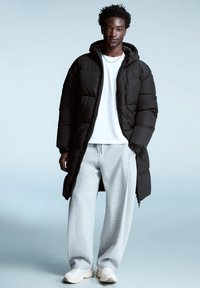 Svart dunjacka med huva och dragkedja, kombinerad med en vit t-shirt och grå sweatpants. Skorna är vita sneakers med tjock sula.