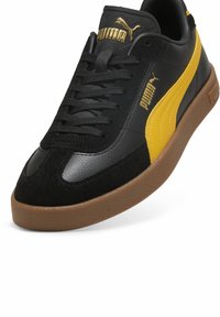 Fekete és sárga sneakers bőr és velúr felsőrésszel, texturált talppal, hagyományos fűzős megoldással és aranyozott logókkal.