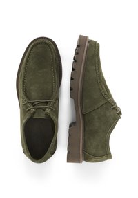 Pantofi din suede verde cu vârf rotund, accente cusute și două gauri pentru șireturile. Aceștia au o talpă din cauciuc maro cu un model striat pentru aderență.