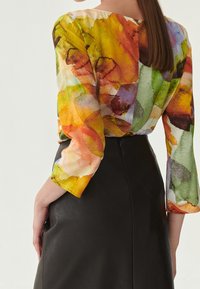Blusa floreale multicolore con maniche a 3/4, realizzata in tessuto leggero. Abbinata a una gonna nera in pelle aderente, con zip laterale.