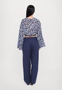 Blue floral cropped blouse with long bell sleeves, paired with high-waisted navy wide-leg trousers. Lightweight, textured fabric.