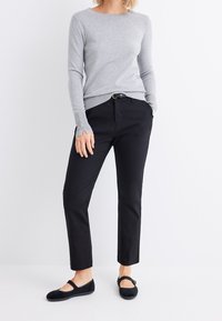 Grau gestrickter Pullover mit langen Ärmeln und detaillierten Bündchen, kombiniert mit schwarzen, gerade geschnittenen Hosen und schwarzen Ballerinas. Schlichtes und sauberes Design.