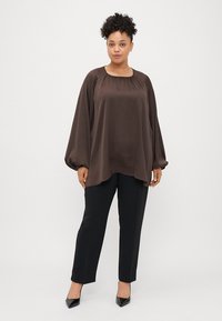 Braune Satinbluse mit rundem Halsausschnitt und Ballonärmeln, kombiniert mit schwarzen, geraden Hosen und schwarzen, spitzen High Heels.