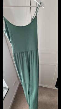 Grüner, gerippter Jumpsuit mit dünnen Trägern, U-Boot-Ausschnitt und lockerer Passform am Unterteil. Weicher Stoff, entworfen für Komfort und Bewegungsfreiheit.