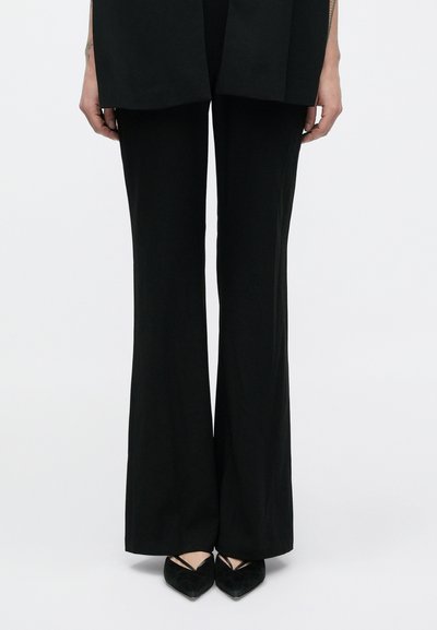 Mustad laiade säärtega püksid sileda tekstuuriga, esiküljel pressvoltidega. Kombineeritud teravate mustade kontsakingadega, millel on ristuvad rihmad.