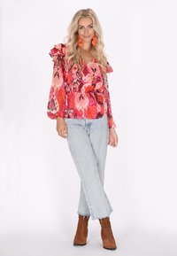 Blusa lunghe maniche colorata e a fantasia con volant; abbinata a jeans azzurri chiari e stivali alla caviglia marroni; orecchini vivaci completano il look.