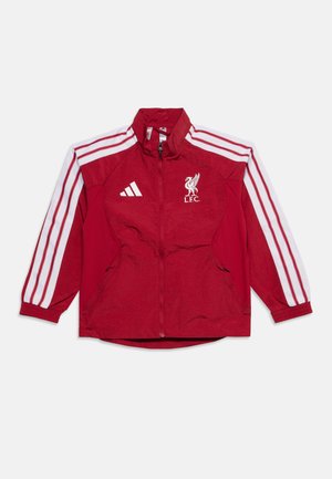 Červená bunda Liverpool FC s bielymi pásikmi Adidas na rukávoch a logami, predný zips a zipsové bočné vrecká, položená na bielom pozadí.