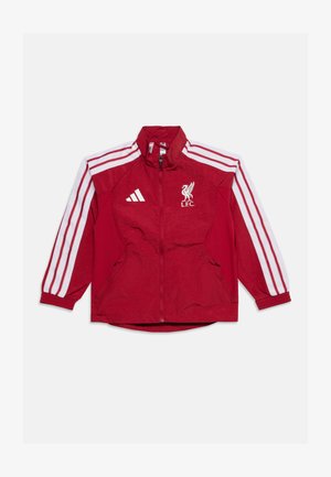 Czerwona kurtka Liverpool FC z białymi pasami Adidas na rękawach i logo, z przednim suwakiem i zamykanymi na zamek bocznymi kieszeniami, rozłożona na białym tle.