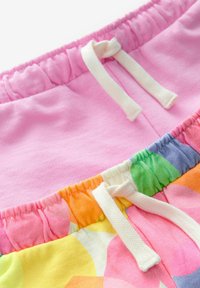 Dve súpravy teplákov s elastickým pásom: jedny jednofarebné ružové a druhé s multicolor kvetinovým vzorom, obe s bielymi šnúrkami.