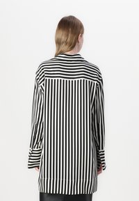 Camisa a rayas blanca y negra de mangas largas, con un corte holgado y un detalle de yugo en la parte posterior. La tela tiene una textura suave y ligera.