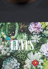 Černá mikina s živým potiskem sukulentů, který zobrazuje různé zelené rostliny, kolibříka a bílé logo "LEVI'S".