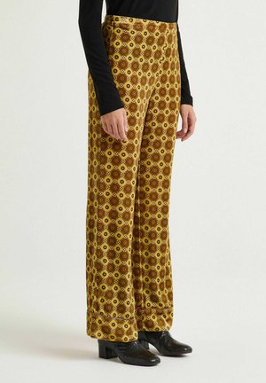 Yellow and brown patterned velvet pants with a flared design, featuring a geometric motif, high waist, and rolled cuffs.