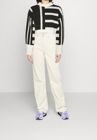 Pull noir et blanc raccourci avec un motif à larges rayures audacieuses, associé à un pantalon large couleur crème. Des baskets gris et violet complètent le look.