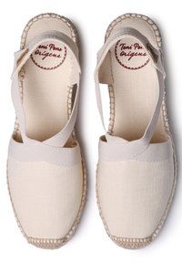 Beige canvas espadrilles with crisscross fabric straps, jute rope sole, and stitched detailing. Comfortable, flat design with a smooth texture.