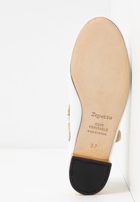 Suola di scarpa in pelle bianca con una soletta beige. Presenta dettagli dorati e un tacco in gomma nera. Testo: "Repetto, Cuir Veritable, Made in France, 37."