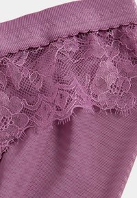 Fioletowa koronkowa bielizna z kwiatowymi wzorami i prążkowanym elastycznym pasem, ukazująca fakturę i delikatne detale przeszyć.