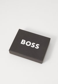 Caixa retangular preta com uma textura suave, apresentando o atrevido logo branco "BOSS" na parte superior. Design simples e moderno.