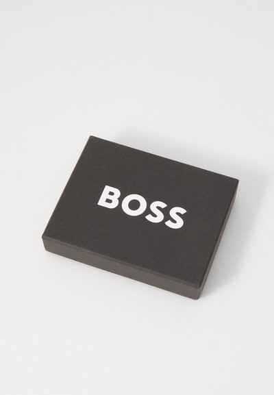 Boîte rectangulaire noire avec une texture lisse, avec la marque "BOSS" en blanc en gras sur le dessus. Design simple et moderne.